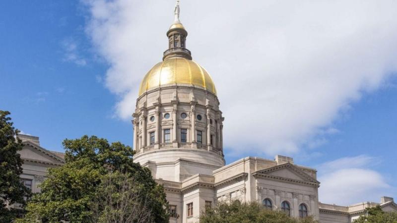 Georgia State Capitol building's gold dome topped with the 'Miss Freedom' statue, with the domed rotunda and portico visible against a partly cloudy sky.