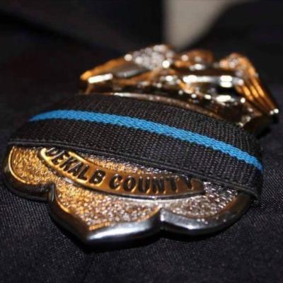 Close-up of a DeKalb County police badge draped with a black band featuring a blue stripe, symbolizing mourning or respect for fallen officers.