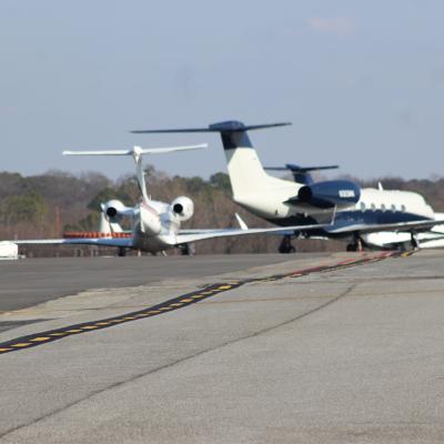 Private jets line up on a runway, with trees in the background under a clear blue sky, conveying a sense of luxury and travel readiness.