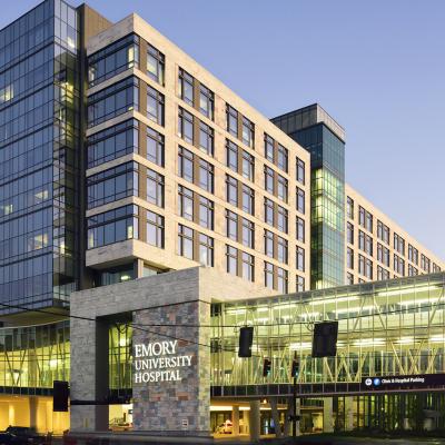 Image of Emory University Hospital with silhouette of cars passing by on the street that has a tree on the left side.