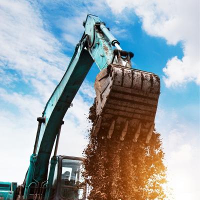 Excavator dumping soil from its bucket against a blue sky