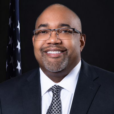 Official portrait of Dr. Ferguson, wearing a dark suit and patterned tie, in front of an American flag.