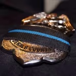 Close-up of a DeKalb County police badge draped with a black band featuring a blue stripe, symbolizing mourning or respect for fallen officers.