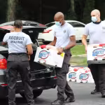 Four police recruits wearing masks load boxes labeled "Cheryl's Best" into a car trunk. The scene is cooperative, with a sense of community service.