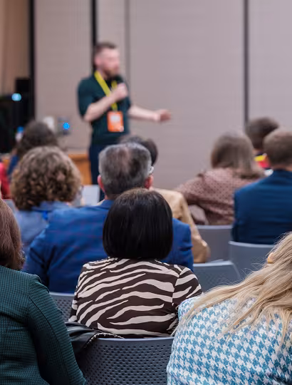 A group of people seated and listening to a speaker presenting at the front of a DeKalb County conference room.