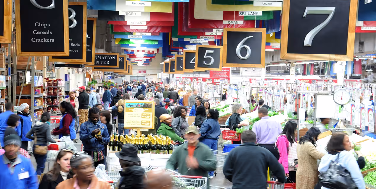A crowded market with numbers lining either side where people can check out. Blurred patrons dart around as they try to navigate the crowded space.