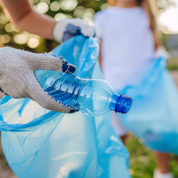 Person wearing gloves places a clear water bottle in a blue trash bag, helping to keep DeKalb County beautiful.