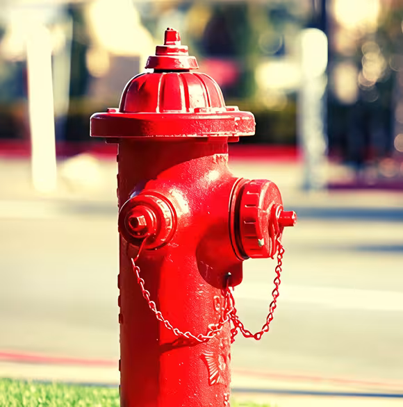 A bright red fire hydrant in a grassy area on the side of the road.