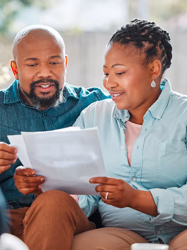 A couple sit next to each other as they go over a pair of papers that the woman is holding.