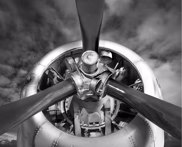 A black and white closeup photo of a propeller on the front of a plane.