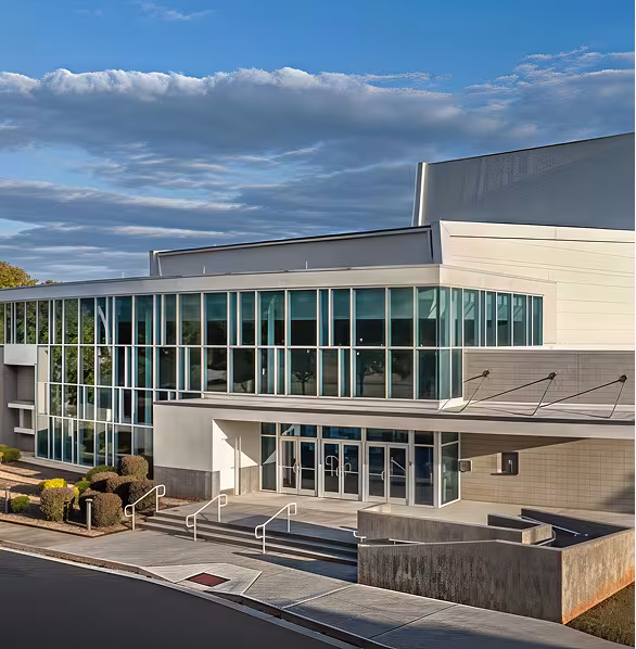 Modern building with large glass windows and clean lines, under a partly cloudy sky. The scene is calm and well-lit, showcasing architectural design.