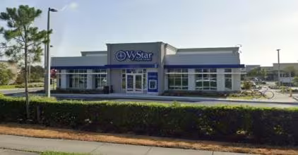 Single-story WyStar Credit Union building with blue accents, large windows, and a landscaped foreground. The sky is clear, suggesting a sunny day.