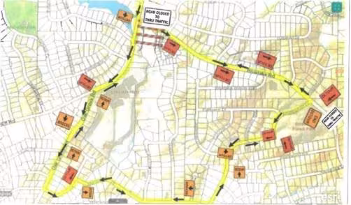 Map with highlighted detour route in yellow, navigating road closures marked by red signs. Arrows indicate alternative paths through a residential area.