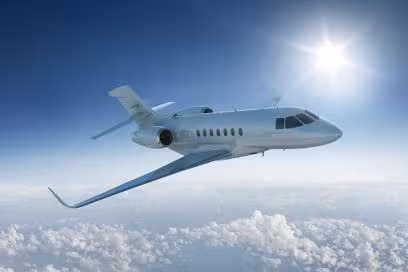 A sleek private jet flies above fluffy white clouds under a clear blue sky. The sun shines brightly, creating a sense of freedom and luxury.
