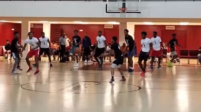 A group of young basketball players in a gym are intensely engaged in a game. The focus and movement convey energy and competition. Spectators watch from the sidelines.