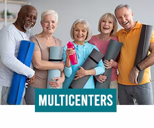 Elderly men and women standing and smiling while holding exercise mats in a room with a shelf in the background.