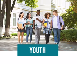 Teenagers walking outside of white school building smiling and talking to each other with trees and a white building in background.