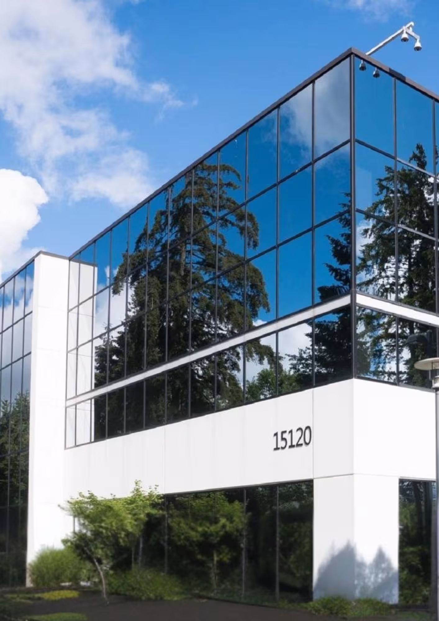 Modern office building with reflective glass façade, featuring the street number 15120. Surrounding trees mirror on the windows under a clear blue sky.