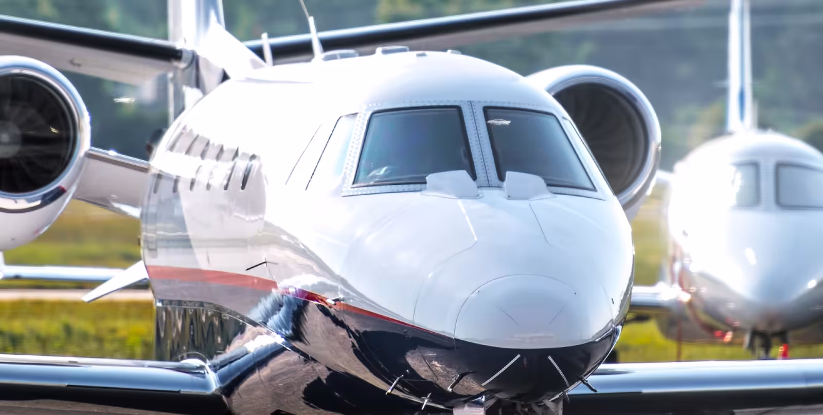 A close-up view of a white private jet parked on a runway with another jet visible in the background.
