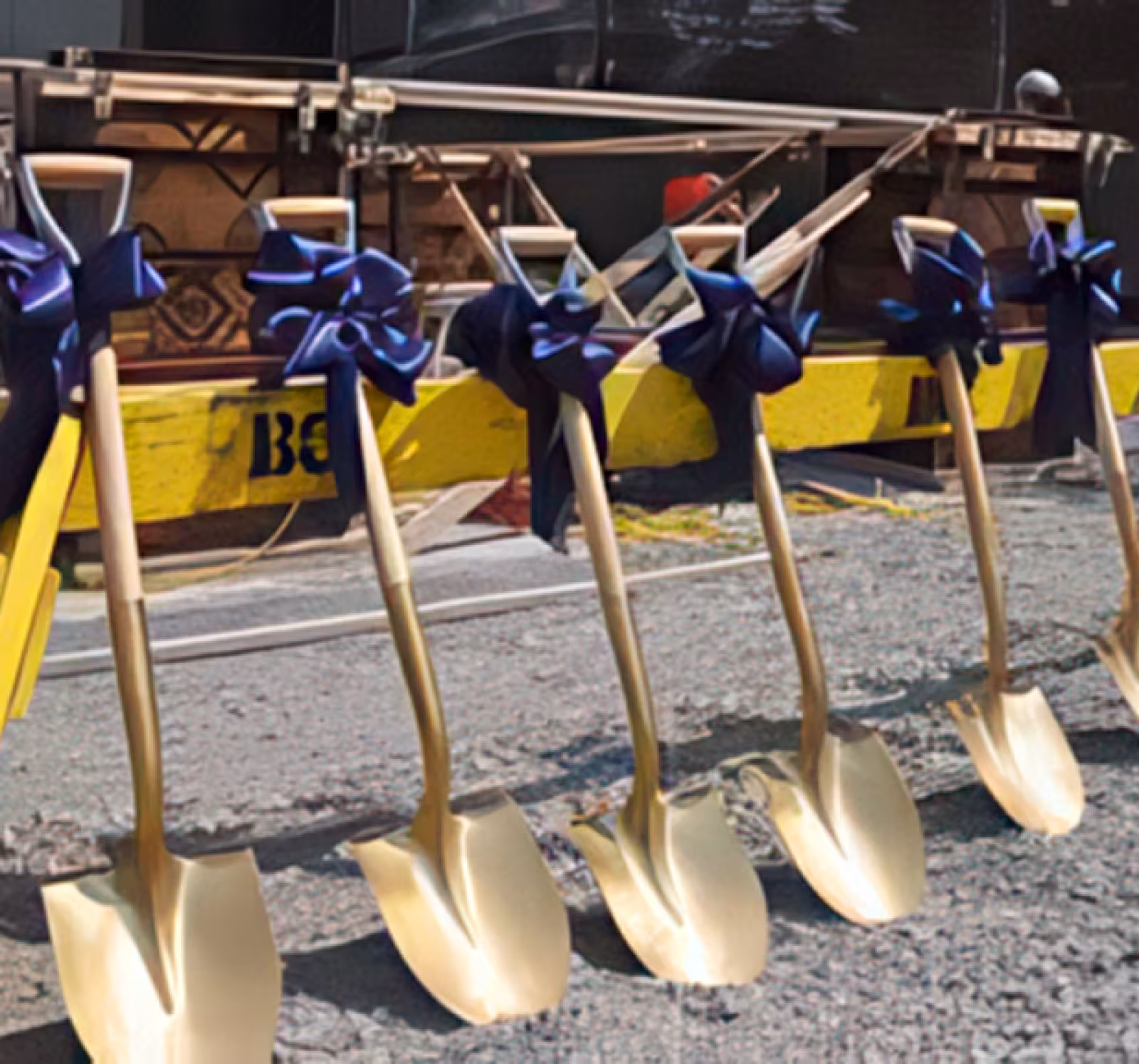 Yellow caution barrier with seven gold shovels leaning against it with blue bows tied around the handles.