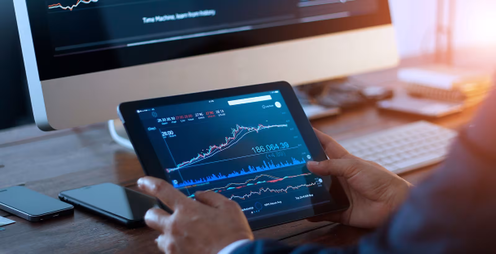 Business person viewing a financial graph on a tablet in an office at sunset.