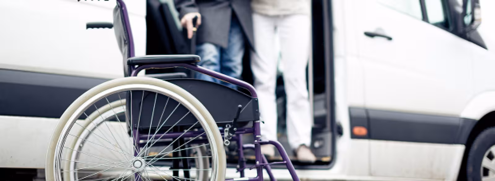 Two people reaching for a manual wheelchair to put it in a white van.