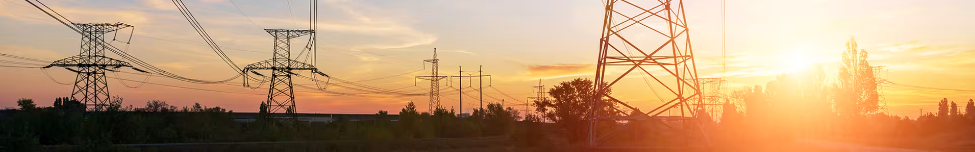A landscape photo of transmission towers with power lines strung between them with a blue and orange sunset.