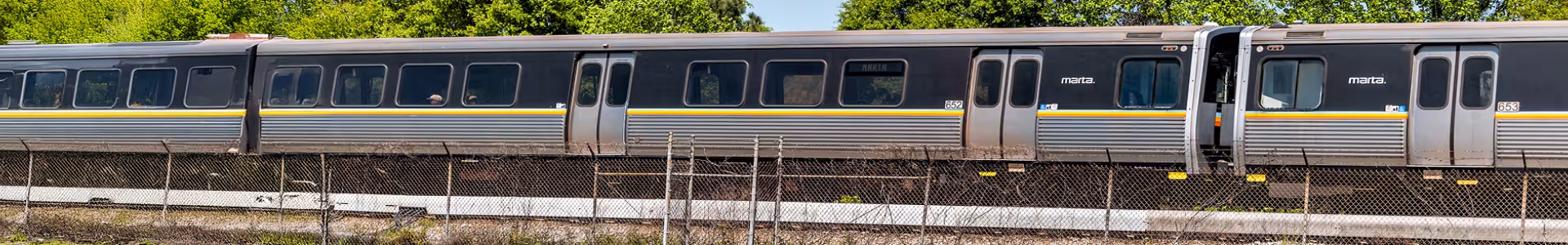 A black train with yellow, orange, and blue stripes going by on tracks with a fence next to it.