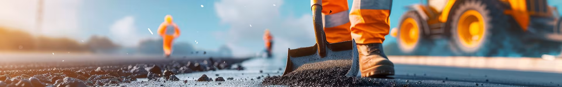 Construction worker with a shovel working on the road with a construction vehicle in the back ground.