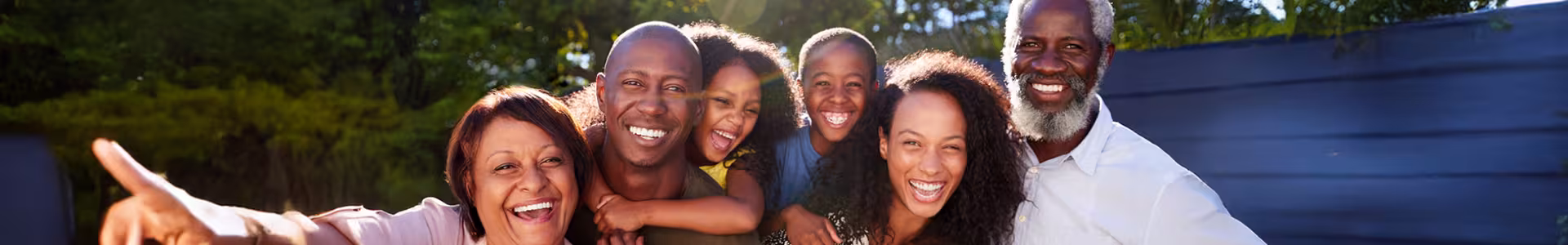 Woman with short grey hair smiling in the middle of a large group of people who are gathering in an outdoor space.