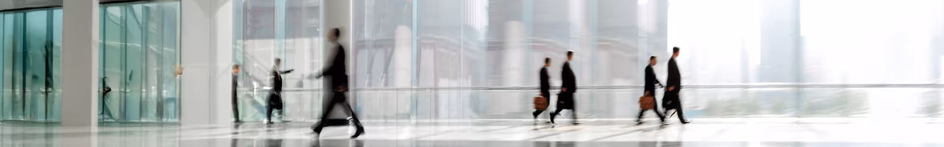 People in business attire walk through a modern, glass-walled building with briefcases.