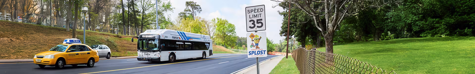 A taxi, bus, and car all drive down a DeKalb County road. Along the road is a 35 MPH speed limit sign and a SPLOST sign underneath.