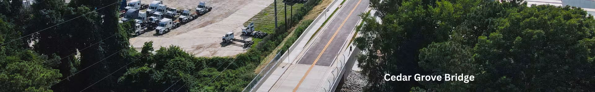 Aerial view of Cedar Grove Bridge spanning railroad tracks, with a two-lane road, sidewalk, and surrounding trucking and industrial lots